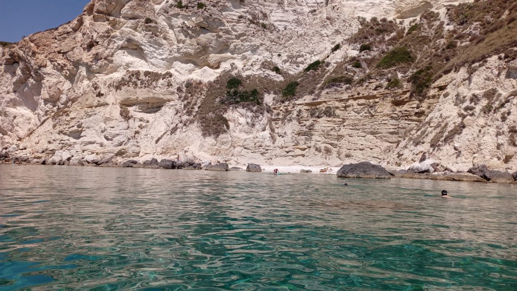 Personas nadando en aguas cristalinas bajo los acantilados de la Sella del Diavolo durante un tour en barco en Cagliari
